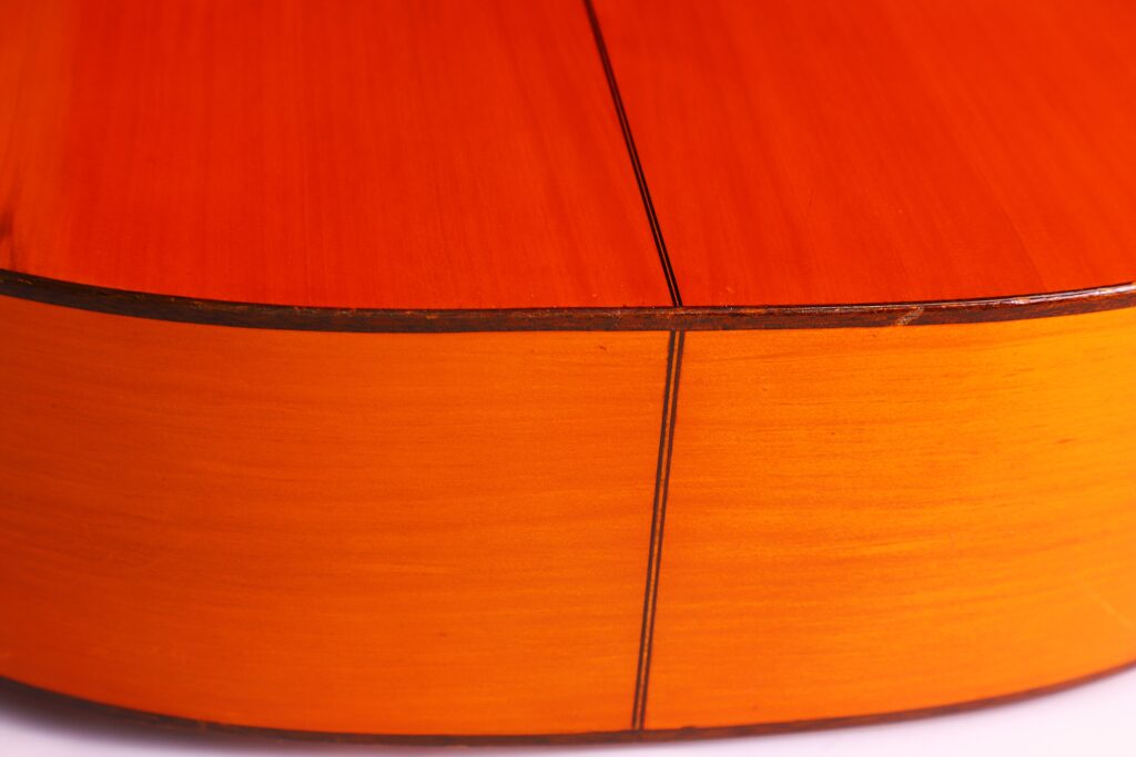 Nahaufnahme Der Rückseite Und Der Seite Der Manuel Reyes 1955 Flamenco-Gitarre. Hervorzuheben Sind Die Glatte Holzoberfläche, Die Sichtbare Naht Und Die Glänzende Orange-Braune Lackierung.