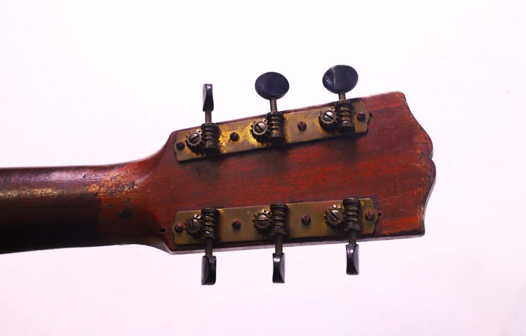 Nahaufnahme Der Gibson L-1 1926 Akustik Gitarre Kopfplattenrückseite Mit Vier Vintage-Stimmwirbeln Mit Metallplatten, Schrauben Und Einer Holzoberfläche Vor Einem Schlichten Weißen Hintergrund.