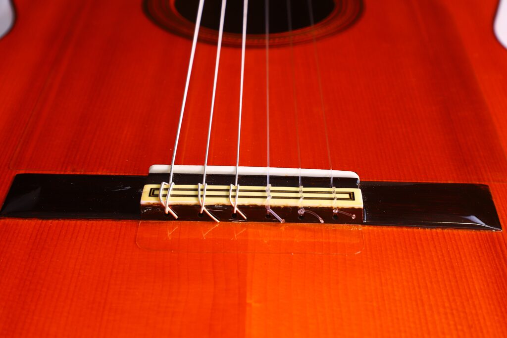 Nahaufnahme Des Stegs Und Der Nylonsaiten Der Manuel Reyes 1955 Flamenco Gitarre, Wobei Die Holzmaserung, Die Stegdetails Und Der Orange-Braune Korpus Hervorgehoben Werden.
