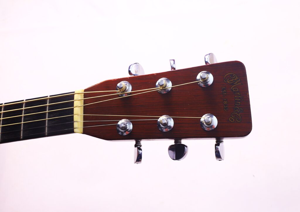 Nahaufnahme Der Kopfplatte Einer Martin D-28 1967 Akustik-Gitarre Mit Sechs Wirbeln Und Saiten Vor Einem Schlichten Hellen Hintergrund. Das Martin &Amp; Co. Logo Und &Quot;Est. 1833&Quot; Sind Auf Der Kopfplatte Aufgedruckt.