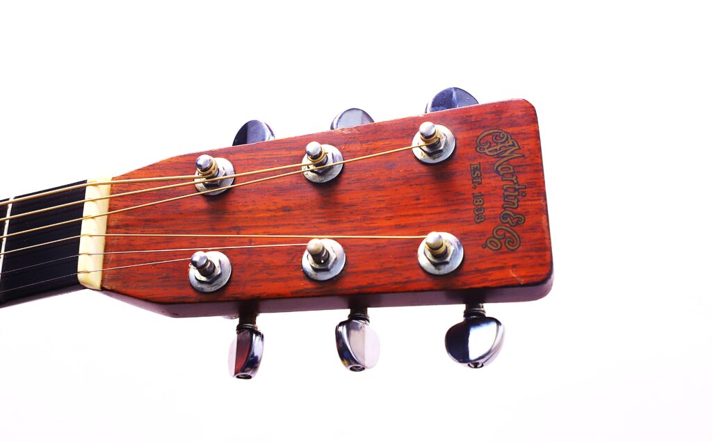 Nahaufnahme Einer Martin D-28 1971 Akustik Gitarre Kopfplatte Mit Sechs Stimmwirbeln, Saiten Und Dem Martin-Logo Auf Poliertem Braunem Holz Vor Weißem Hintergrund.