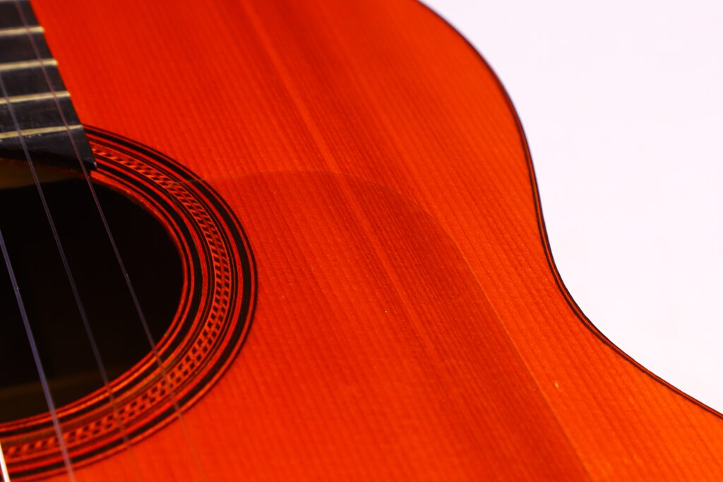 Nahaufnahme Einer Flamenco-Gitarre Von Manuel Reyes Aus Dem Jahr 1955. Hervorzuheben Sind Die Detaillierte Holzmaserung, Die Filigrane Rosette Um Das Schallloch Und Ein Teil Des Dunklen Griffbretts Vor Weißem Hintergrund.