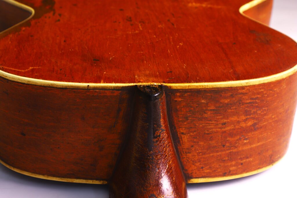 Nahaufnahme Der Rückseite Einer Gibson L-1 1926 Akustik-Gitarre, Wobei Die Abgenutzte Hals-Korpus-Verbindung Hervorgehoben Wird. Die Oberfläche Weist Kratzer Und Verblassen Auf, Mit Deutlichen Anzeichen Von Alter Und Gebrauch.