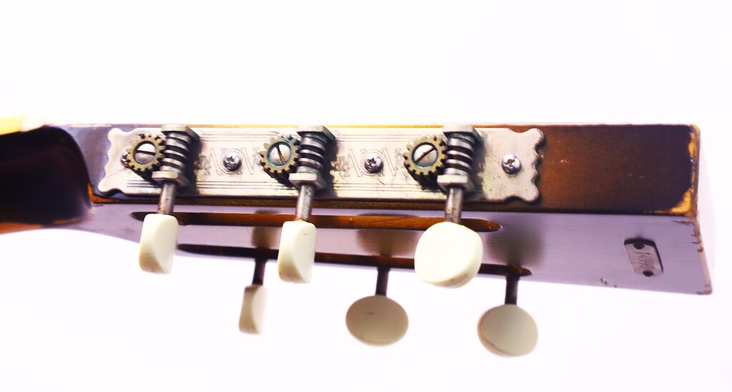 Nahaufnahme Der Stimmwirbel An Der Kopfplatte Einer National Reso-Phonic Style O 2009 Akustikgitarre, Mit Einer Metallplatte Und Weißen Stimmknöpfen Vor Einem Hellen, Weißen Hintergrund.