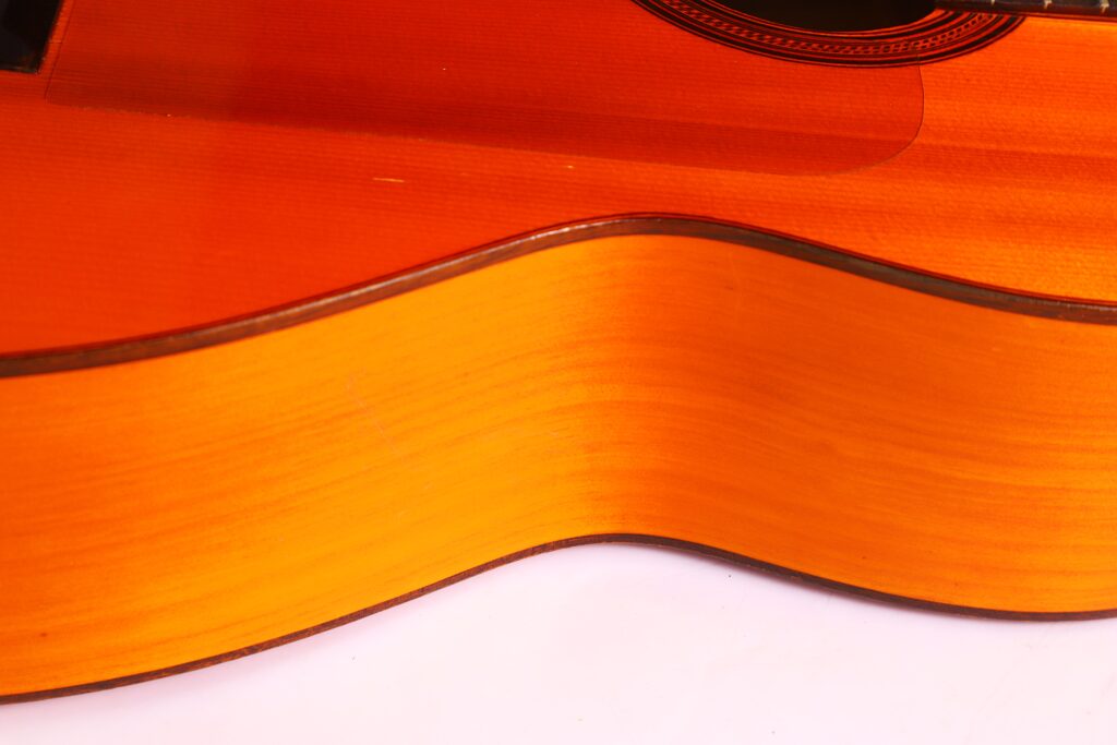 Nahaufnahme Der Seite Und Des Korpus Einer Flamenco-Gitarre Von Manuel Reyes Aus Dem Jahr 1955. Hervorzuheben Sind Die Glatte Holzoberfläche Und Die Natürliche Braun-Orangefarbene Lackierung Vor Einem Weißen Hintergrund.