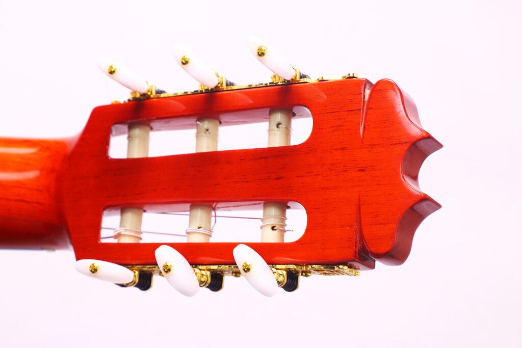 Nahaufnahme Der Kopfplatte Einer Hermanos Conde 1990 Paco De Lucia Special Flamenco Gitarre Mit Weißen Stimmwirbeln, Goldenen Beschlägen Und Dekorativen Schnitzereien Auf Rötlichem Holz Vor Einem Schlichten Hellen Hintergrund.