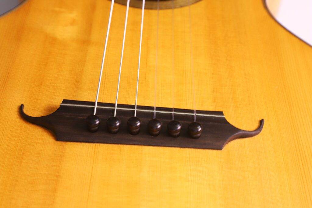 Nahaufnahme Des Stegs Und Der Saiten Der Grobert Romantikgitarre 2016 Von Yoann Charbonnier. Hervorzuheben Sind Die Maserung Des Holzkorpus Und Der Dunkle Steg Mit Sechs Schwarzen Stiften Zur Befestigung Der Saiten.