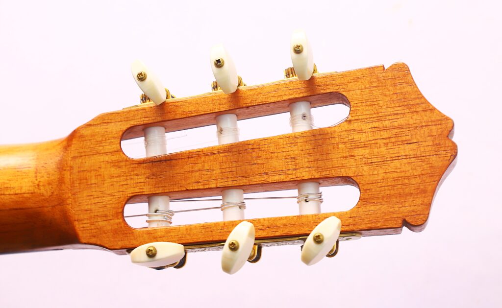 Nahaufnahme Der Kopfplatte Der Oscar Orozco 2023 Santos Hernández Flamenco-Gitarre Mit Sechs Weißen Stiftwirbeln Und Durch Hölzerne Schlitze Gefädelten Saiten Vor Einem Hellen Hintergrund.