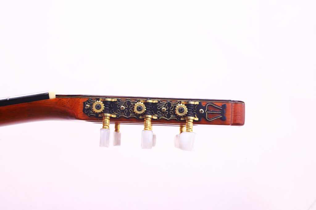 Nahaufnahme Der Kopfplatte Der José Ramírez Rb-A 636 Klassische Gitarre, Die Verschnörkelte Goldene Stimmwirbel Mit Weißen Knöpfen Vor Einem Schlichten, Hellen Hintergrund Aufweist.