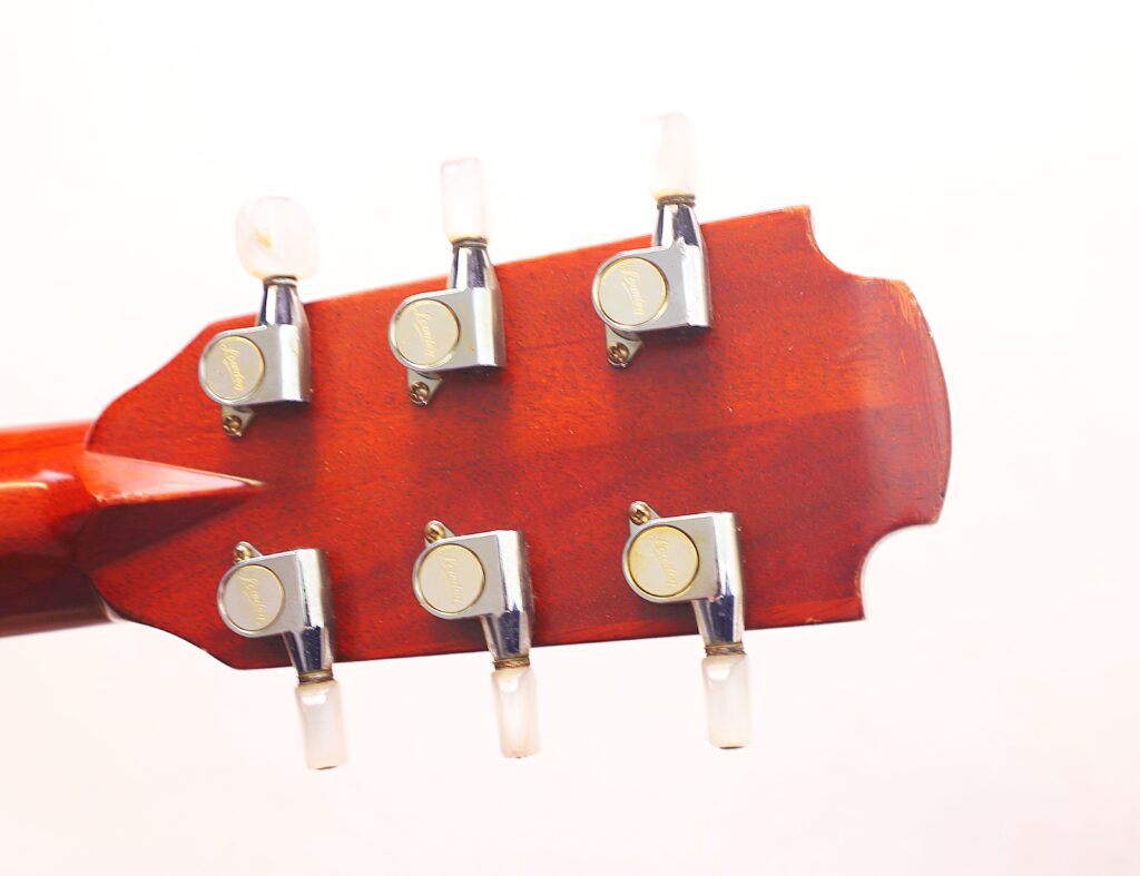 Nahaufnahme Der Rückseite Einer Lowden F-9 1980 Akustikgitarre, Die Sechs Silberne Stimmwirbel (Drei Pro Seite) Vor Einem Schlichten Weißen Hintergrund Zeigt.