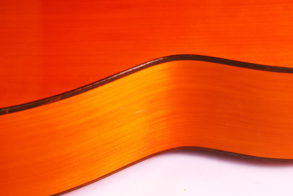 Nahaufnahme Der Seite Und Des Randes Einer Flamenco-Gitarre Von Manuel Reyes Aus Dem Jahr 1955. Hervorzuheben Ist Die Glatte Orangefarbene Und Braune Holzmaserung Mit Gewellten Konturen Vor Einem Weißen Hintergrund.