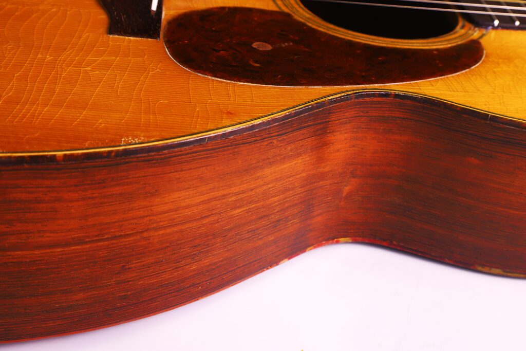 Nahaufnahme Der Seite Und Des Korpus Einer Martin 000-21 Akustikgitarre Von 1947, Die Die Holzmaserung, Feine Kratzer, Einen Teil Der Decke Und Des Schlagbretts Zeigt, Wobei Die Gitarrensaiten An Der Decke Teilweise Sichtbar Sind.