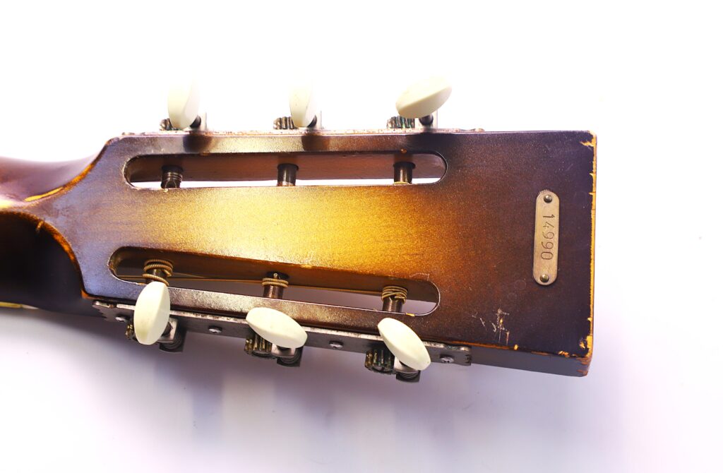 Nahaufnahme Einer National Reso-Phonic Style O 2009 Akustik Gitarre Kopfplatte Mit Weißen Stimmwirbeln Und Sichtbaren Gebrauchsspuren. An Der Kopfplatte Befindet Sich Ein Metallschild. Der Hintergrund Ist Weiß.