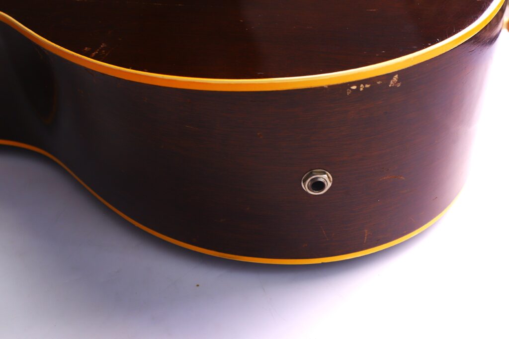 Nahaufnahme Der Seite Einer Gibson J-45 1957 Akustik Gitarre, Dunkelbraun Mit Gelbem Rand Und Klinkeneingang, Mit Kratzern Und Abnutzung Des Holzes.