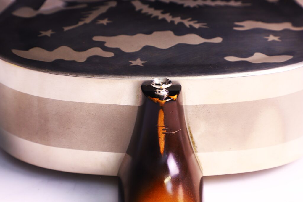 Nahaufnahme Der Rückseite Einer National Reso-Phonic Style O 2009 Akustikgitarre, Die Den Übergang Zwischen Hals Und Korpus Hervorhebt. Die Glänzende Metalloberfläche Ist Mit Sternen, Wolken Und Einem Baummuster Graviert.