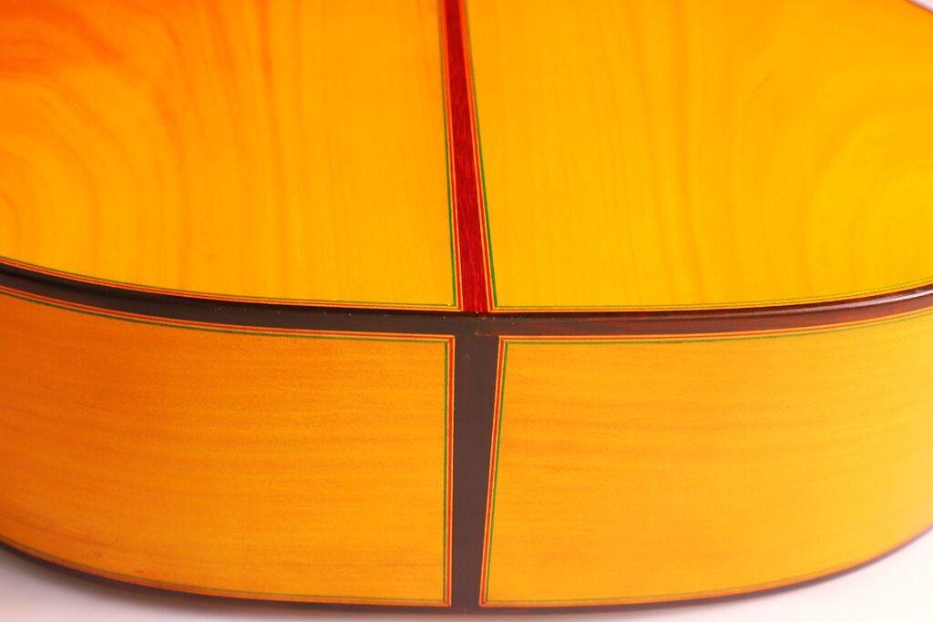 Nahaufnahme Der Rückseite Der Graciliano Perez 2025 Flamenco-Gitarre. Hervorzuheben Sind Die Gelbe Lackierung, Die Sichtbare Holzmaserung, Der Dunkle Mittelstreifen Und Die Detaillierte Randeinfassung.