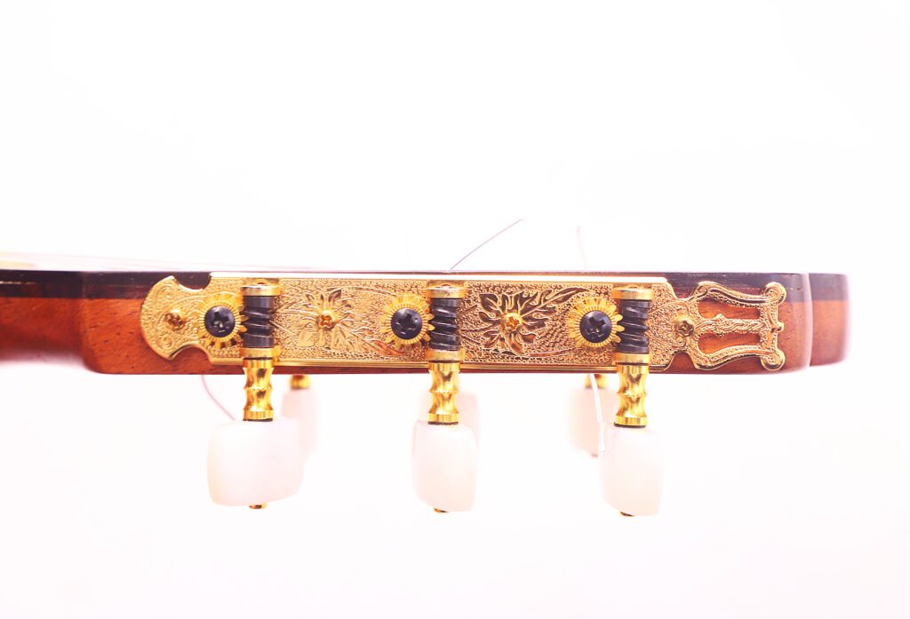 Nahaufnahme Der Kopfplatte Der Vicente Tatay Alabau 1920 Klassische Gitarre, Die Mit Goldenen Stimmwirbeln Und Weißen Knöpfen Verziert Ist Und Aufwändige Gravuren Auf Der Metallplatte Aufweist.