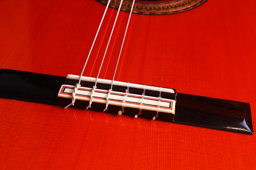 Nahaufnahme Des Stegs Und Der Saiten Der Hermanos Conde 1990 Paco De Lucia Special Flamenco Gitarre Auf Dem Polierten, Rötlich-Braunen Holzkorpus, Die Die Komplizierten Stegdetails Und Die Saitenverankerung Hervorheben.