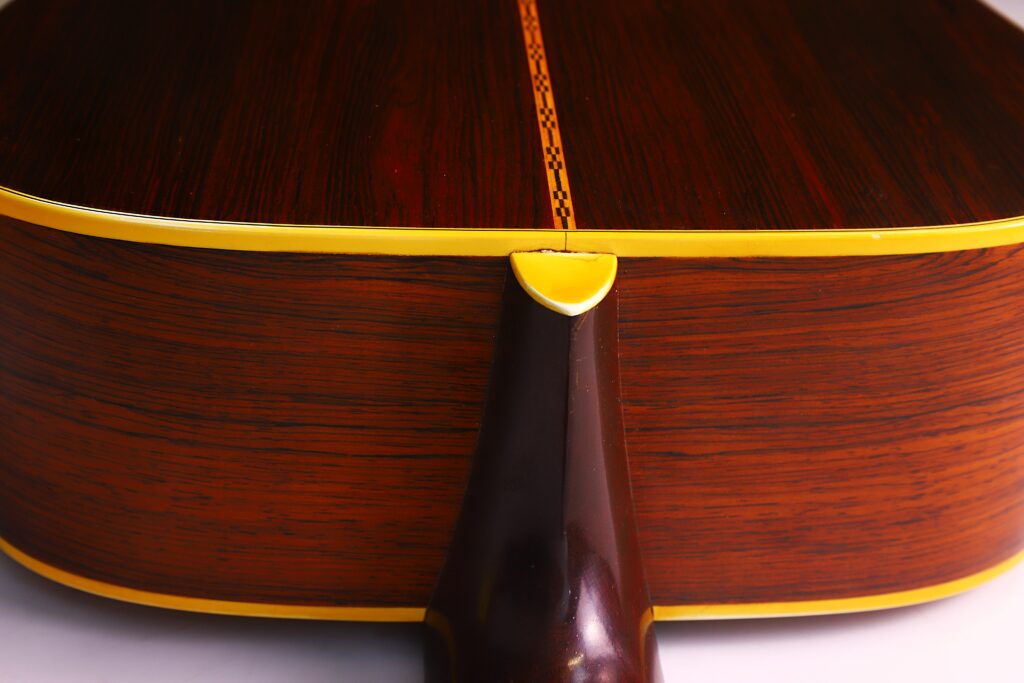 Nahaufnahme Des Bodens Der Martin D-28 1967 Akustik Gitarre Mit Poliertem, Dunklem Holz, Einer Dekorativen Einlage, Einer Gelben Einfassung Und Einer Teilansicht Des Halsgelenks.