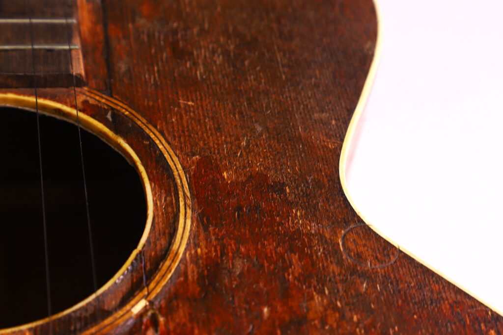 Nahaufnahme Eines Abgenutzten Gibson L-1 1926 Akustikgitarrenkorpus, Mit Schallloch, Sichtbarer Holzmaserung Und Kratzern, Mit Einem Teil Eines Weißen Hintergrunds Auf Der Rechten Seite.