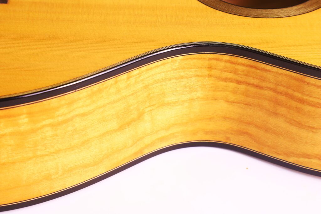 Nahaufnahme Der Zarge Und Des Korpus Der Grobert Romantikgitarre 2016 Von Yoann Charbonnier Mit Glatter, Glänzender, Heller Holzmaserung Und Dunkler Zierleiste, Mit Einem Teil Des Schalllochs Oben Rechts Vor Weißem Hintergrund.