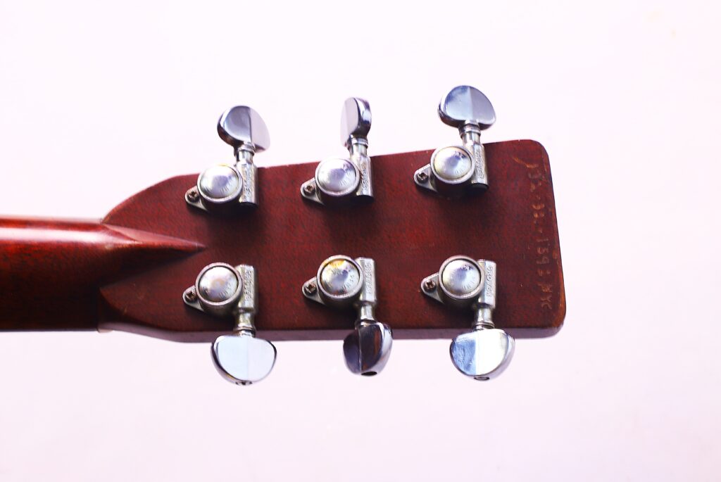 Nahaufnahme Der Rückseite Der Kopfplatte Einer Martin D-28 Akustikgitarre Von 1971 Mit Sechs Metallstimmwirbeln. Die Rötlich-Braune Holzoberfläche Weist Seitlich Schwache Markierungen Auf, Die Vor Einem Schlichten, Hellen Hintergrund Stehen.