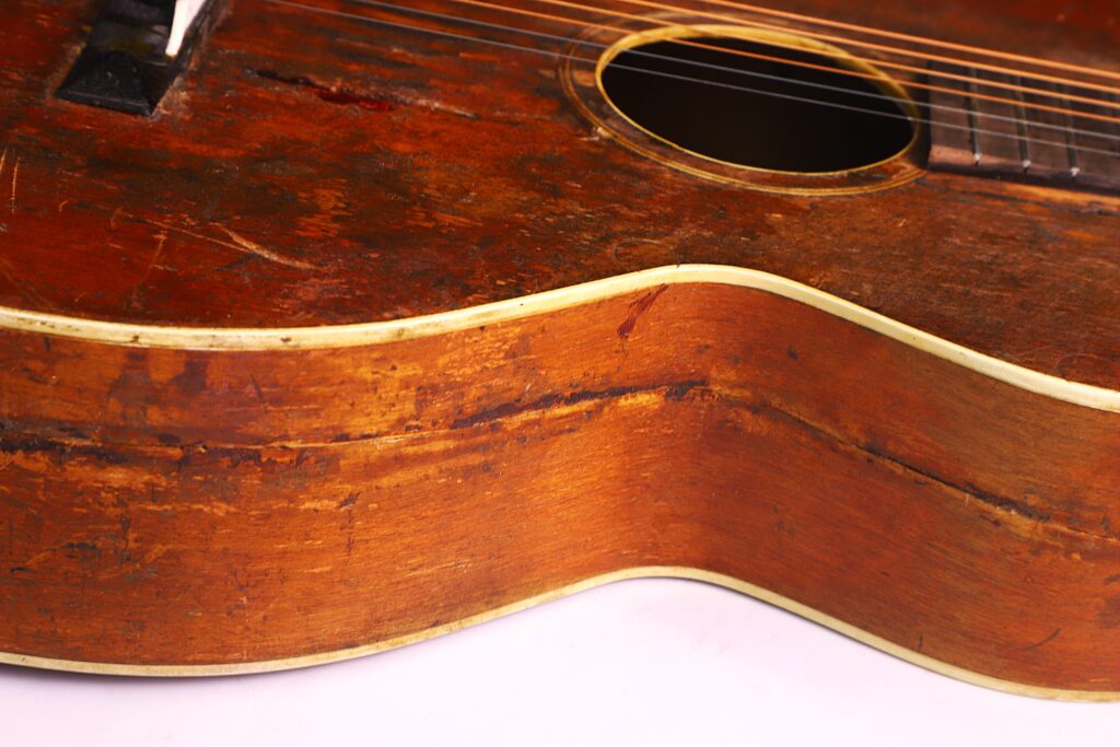 Eine Nahaufnahme Der Gibson L-1 1926 Akustik Gitarre Zeigt Kratzer, Beulen Und Verfärbungen Auf Dem Holzkorpus, Die Den Vintage-Charakter Und Den Häufigen Gebrauch Unterstreichen.