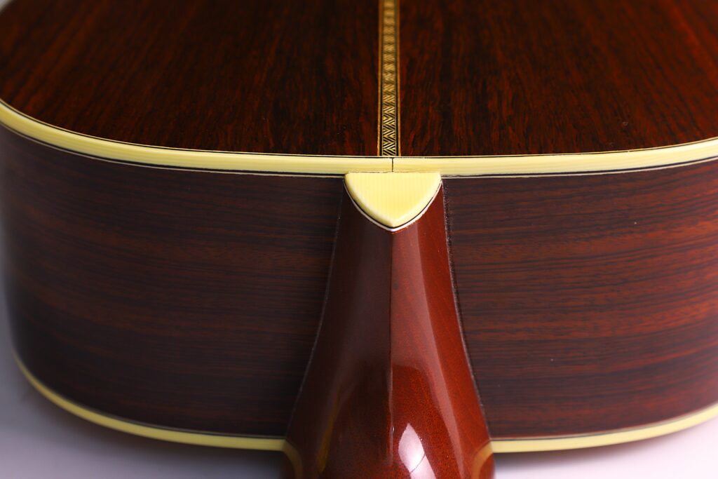 Nahaufnahme Des Halsgelenks Einer Martin 0-28 Ian Anderson Akustik Gitarre Mit Poliertem Dunklem Holz, Einem Dekorativen Einlagenstreifen Und Cremefarbenem Binding Entlang Der Kanten.