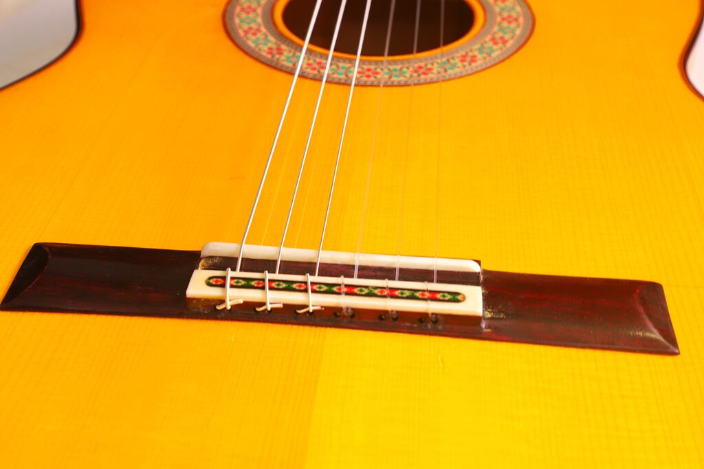 Nahaufnahme Des Stegs Und Der Saiten Der Graciliano Perez 2025 Flamenco-Gitarre, Die Den Gelben Holzkorpus Und Die Verzierten Details In Der Nähe Des Schalllochs Hervorheben.