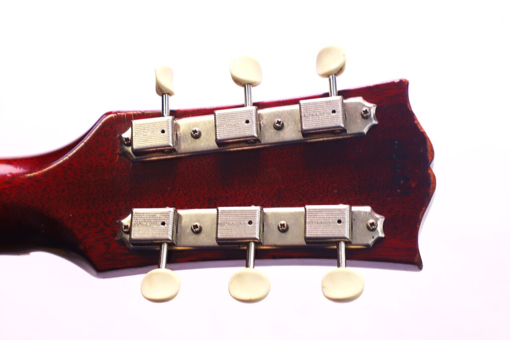 Nahaufnahme Der Rückseite Einer Gibson J-45 1962 Akustik Gitarre Mit Sechs Metallstimmwirbeln Und Weißen Stimmknöpfen Vor Weißem Hintergrund.