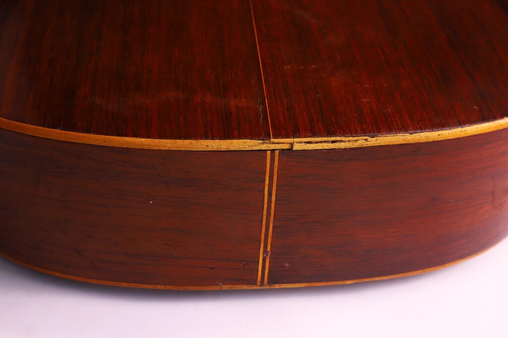 Primo piano del retro e del lato della chitarra classica Salvador Ibanez 1900, con tonalità di legno marrone caldo, arrossature gialle e cuciture visibili dove le parti in legno sono unite.