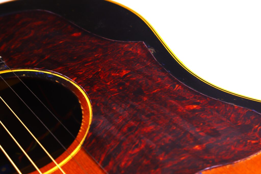 Nahaufnahme Des Korpus Einer Gibson J-45 1957 Akustik-Gitarre, Wobei Die Saiten, Das Schallloch Und Das Rotbraun Marmorierte Schlagbrett Mit Gelber Und Schwarzer Zierleiste Vor Weißem Hintergrund Hervorgehoben Werden.