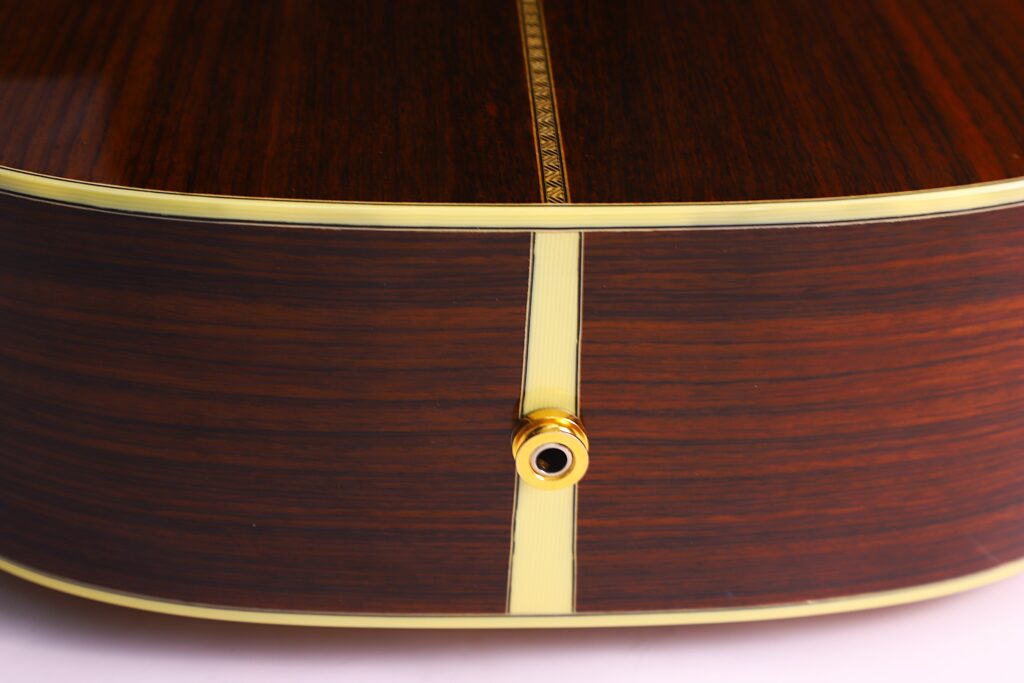 Nahaufnahme Von Zarge Und Boden Der Martin 0-28 Ian Anderson Akustik Gitarre Mit Goldenem Gurtknopf, Cremefarbenem Binding Mit Ziereinlage Und Dunkelbrauner Holzoberfläche Mit Sichtbarer Maserung.