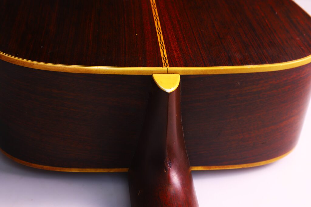 Nahaufnahme Des Bodens Und Des Halses Einer Martin D-28 1971 Akustik-Gitarre Mit Dunklem Holz, Gelber Zierleiste Und Mittelfalzeinlage. Der Helle Hintergrund Ist Unscharf.