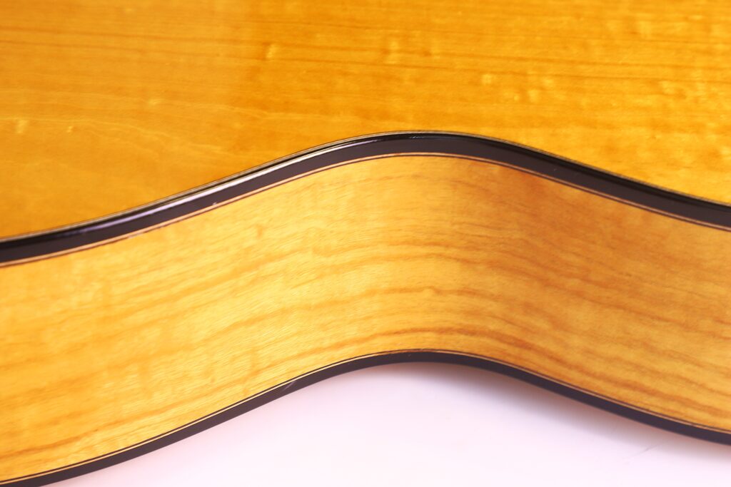 Nahaufnahme Der Seite Der Grobert Romantikgitarre 2016 Von Yoann Charbonnier, Die Die Helle Holzmaserung, Die Dunkle Zierleiste Und Die Glatte, Geschwungene Form Des Gitarrenkörpers Zeigt.