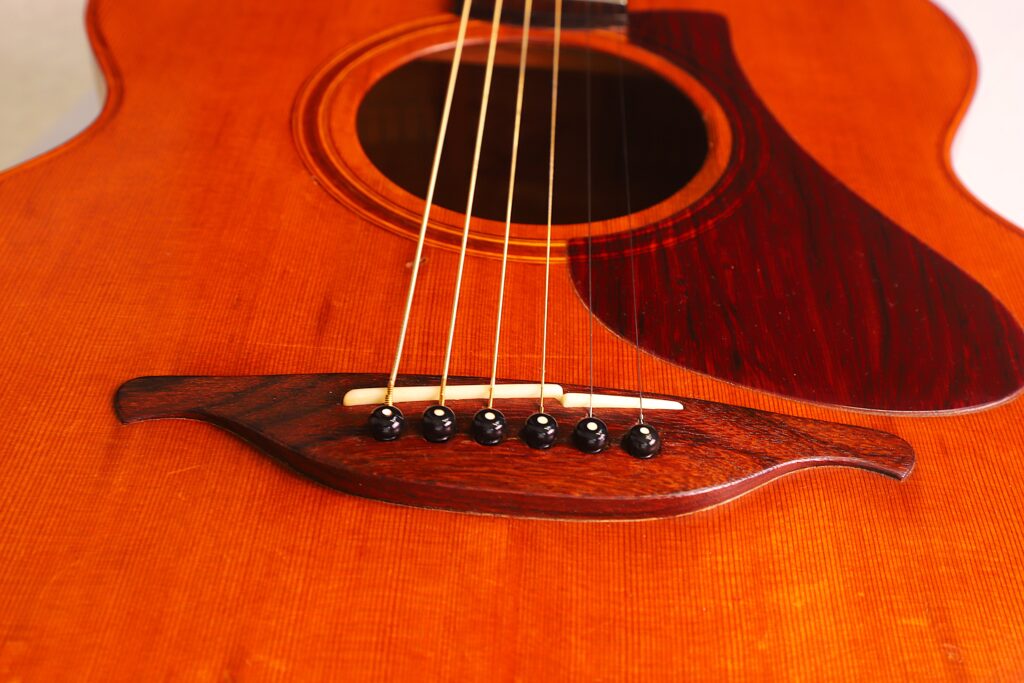 Nahaufnahme Der Lowden F-9 1980 Akustik-Gitarre, Die Den Holzkorpus, Den Steg, Die Saiten Und Das Schlagbrett Mit Satten Braun-Orangen Tönen Und Sichtbarer Holzmaserung Hervorhebt.