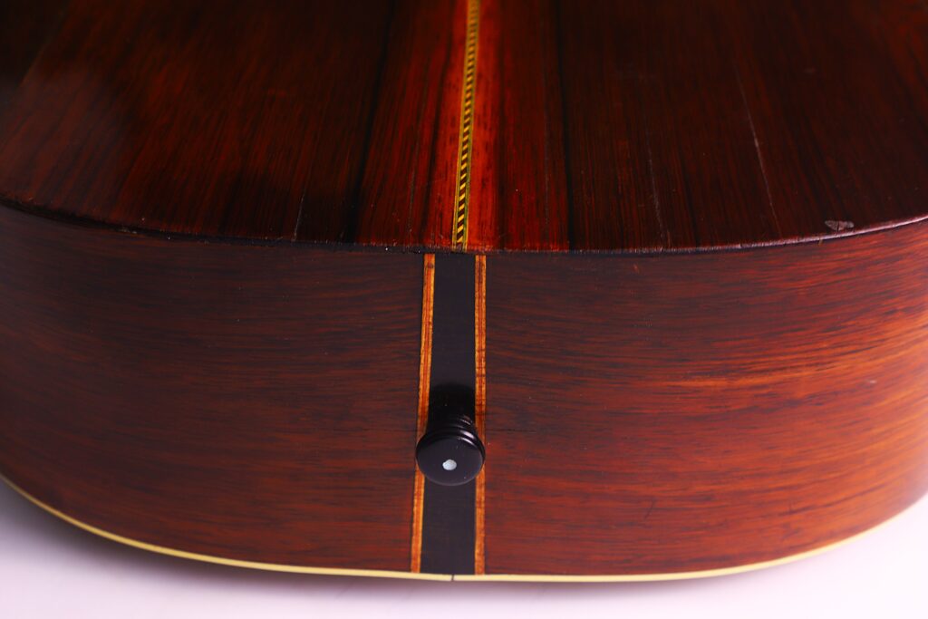 Nahaufnahme Des Bodens Und Der Zarge Der Washburn 1894 Parlor Akustik Gitarre Mit Holzmaserung, Dekorativer Mittelnaht, Gelber Einfassung Und Einem Schwarzen Gurtknopf An Der Unterseite.