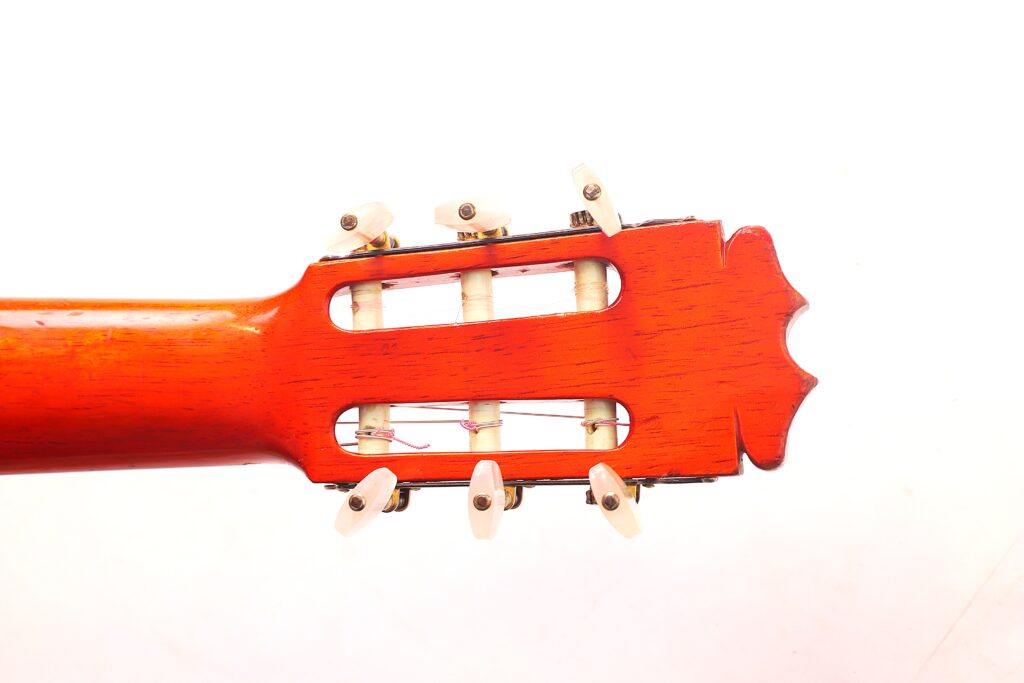 Nahaufnahme Der Kopfplatte Einer Faustino Conde Flamenco-Gitarre Von Hermanos Conde Aus Dem Jahr 1983 Mit Rötlicher Holzoberfläche Und Weißen Stimmwirbeln Vor Weißem Hintergrund.