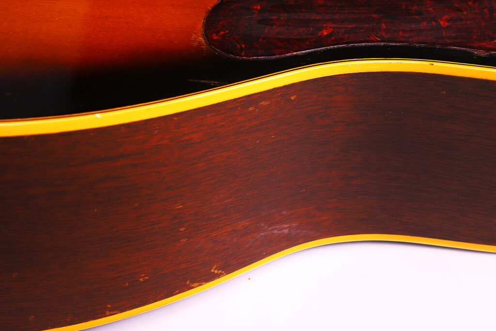 Nahaufnahme Der Gibson J-45 1957 Akustik Gitarre, Die Die Braune Holzmaserung, Das Gelbe Binding Und Den Glänzenden Dunklen Korpus Vor Weißem Hintergrund Hervorhebt.