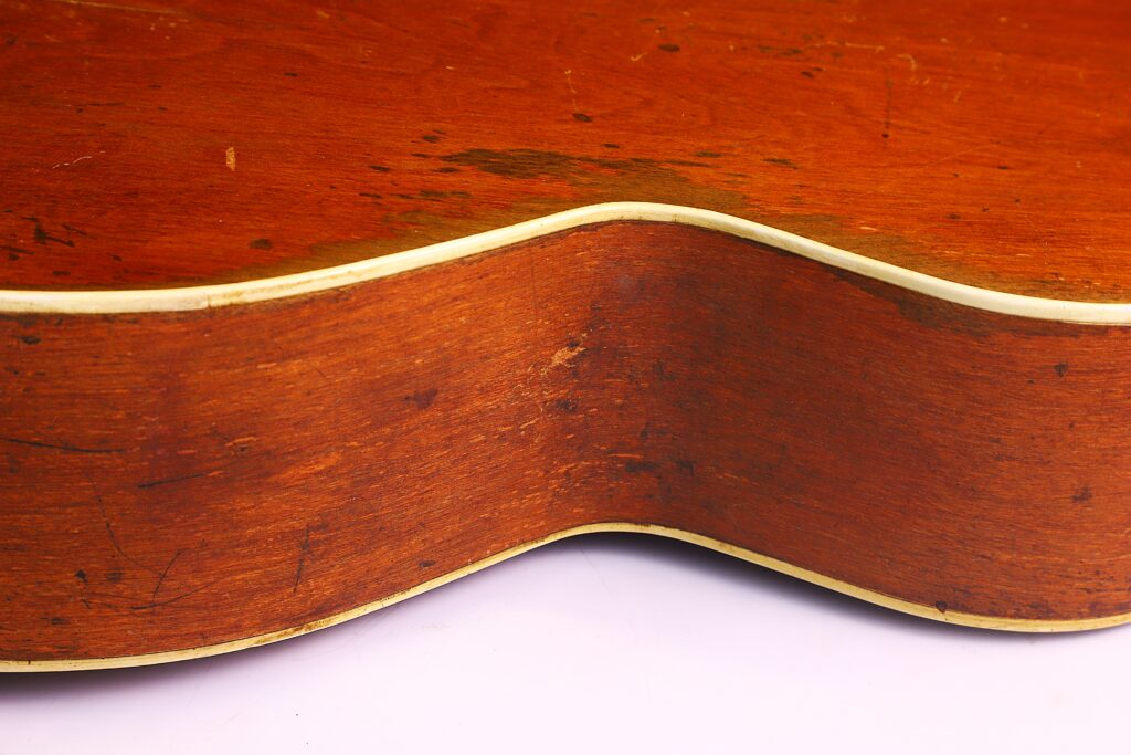 Nahaufnahme Der Holzseite Einer Gibson L-1 1926 Akustik-Gitarre Mit Leicht Abgenutztem Rotbraunem Finish, Cremefarbener Kante Und Sichtbaren Oberflächenkratzern, Die Auf Den Alten Gebrauch Hinweisen.
