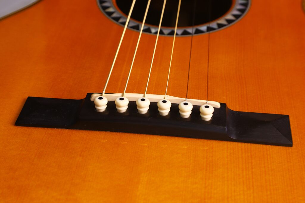 Nahaufnahme Des Stegs Der Martin 0-28 Ian Anderson Akustik Gitarre Mit Sechs Weißen Stiften, Die Die Saiten Auf Dem Glänzenden Holzkorpus Fixieren.