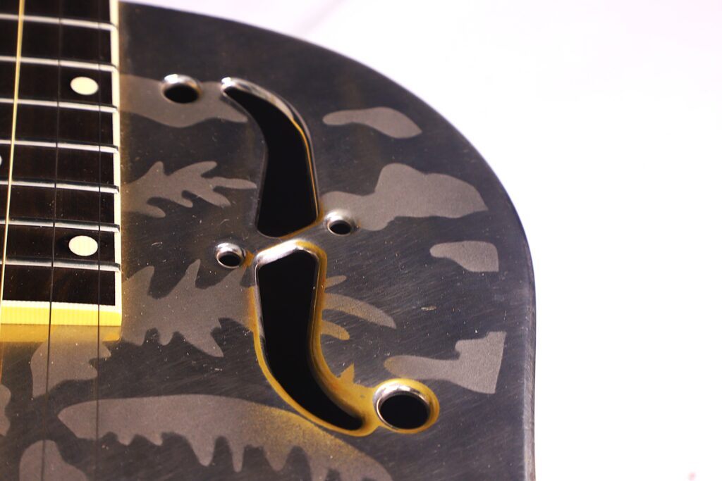 Nahaufnahme Des Korpus Einer National Reso-Phonic Style O 2009 Akustikgitarre Mit Tarnmuster, Die Einen Teil Des Halses, Des Griffbretts, Des Schalllochs Und Der Metallteile Vor Einem Weißen Hintergrund Zeigt.