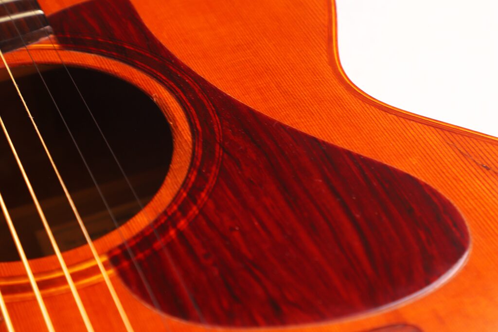 Nahaufnahme Einer Lowden F-9 1980 Akustikgitarre Mit Schallloch, Saiten Und Rotbraunem Schlagbrett Auf Einem Polierten Holzkorpus Vor Einem Teilweise Weißen Hintergrund.