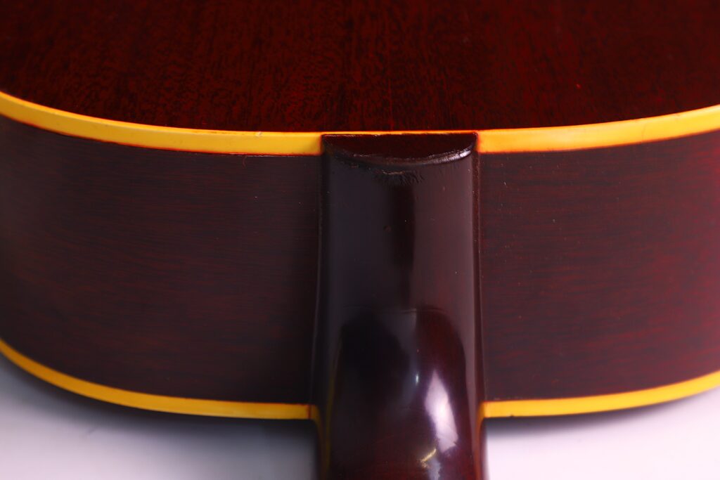Nahaufnahme Der Rückseite Einer Gibson J-45 1962 Akustik-Gitarre, Die Eine Glänzende Dunkelbraune Holzoberfläche Mit Gelben Rändern Und Details Am Halsgelenk Aufweist, Wo Der Hals Auf Den Korpus Trifft.