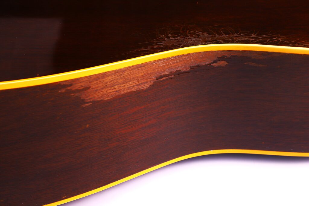 Nahaufnahme Der Seite Einer Gibson J-45 1957 Akustik-Gitarre In Dunkelbraun Mit Gelbem Einband, Wobei Ein Großer Bereich Hervorgehoben Wird, In Dem Die Lackierung Abgenutzt, Verkratzt Und Verblasst Ist.