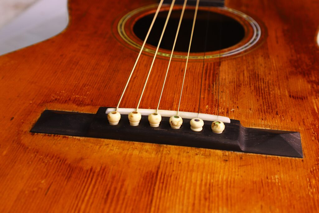 Nahaufnahme Des Stegs Und Der Saiten Der Martin 0-30 1917 Akustik Gitarre. Man Erkennt Die Gealterte Holzoberfläche Und Die Weißen Stegstifte, Die Die Saiten Sicher Halten.