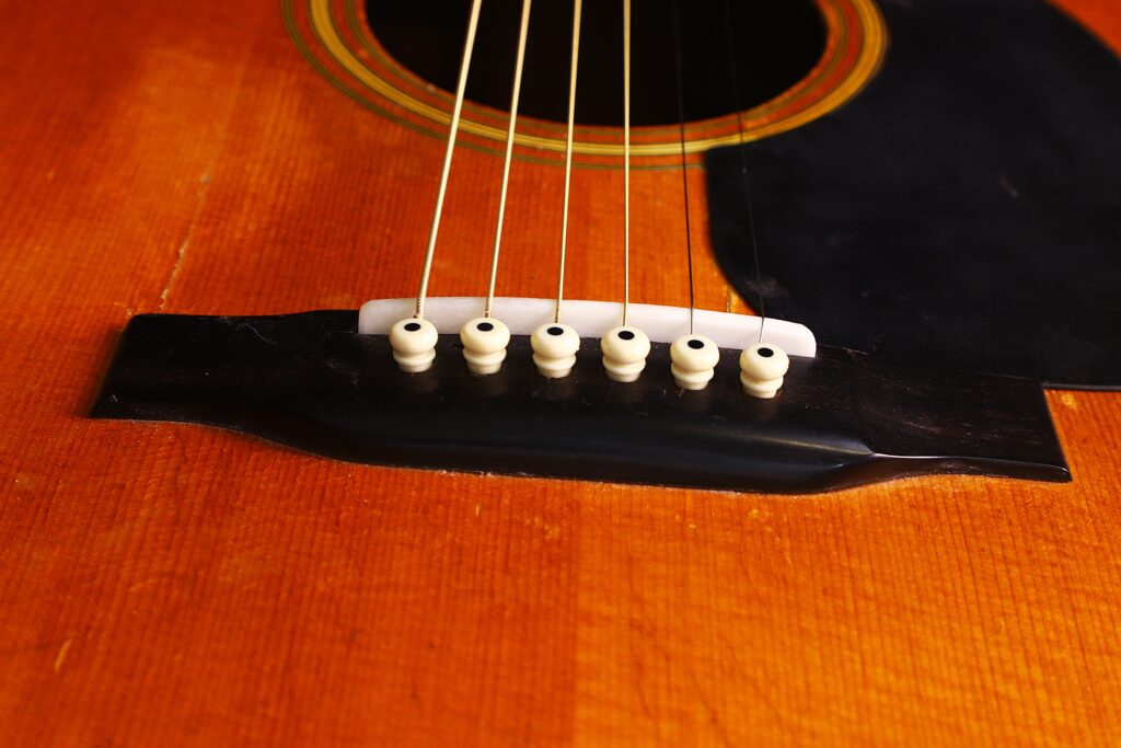 Nahaufnahme Des Stegs Und Der Saiten Einer Martin D-28 1971 Akustik Gitarre. Hervorzuheben Sind Die Weißen Stegstifte, Der Sattel, Ein Teil Des Hölzernen Gitarrenkorpus Und Die Gespannten Saiten, Die Nach Oben Aus Dem Rahmen Laufen.