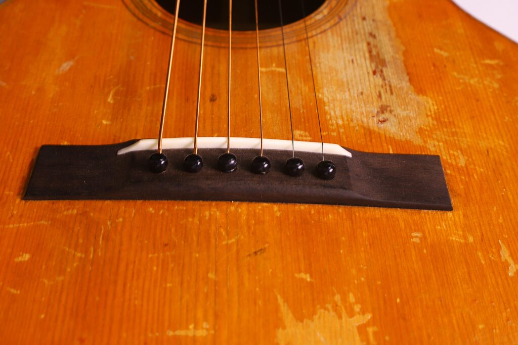 Nahaufnahme Des Stegs Und Der Saiten Einer Martin 0-18 1926 Akustik Gitarre. Hervorzuheben Sind Das Abgenutzte, Zerkratzte Holz Und Die Sechs Saitenwirbel, Mit Denen Die Saiten Im Vintage-Akustik-Korpus Verankert Sind.