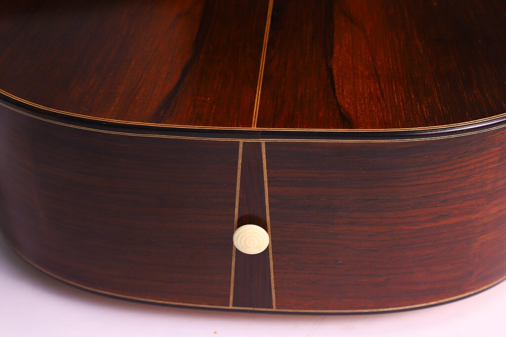 베른하르트 크레세 1999 파노르모 로맨틱 기타의 뒷면과 측면을 클로즈업한 사진입니다. 짙은 나뭇결, 장식용 인레이, 중앙 하단의 흰색 스트랩 버튼이 강조되어야 합니다.