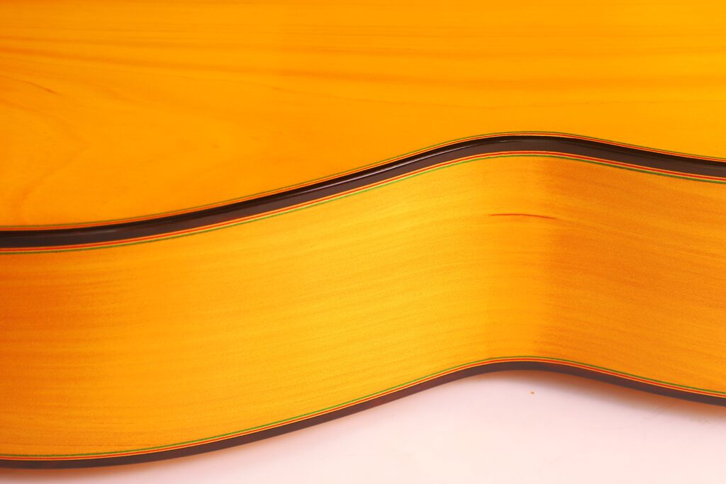 Seitenansicht Der Graciliano Perez 2025 Flamenco-Gitarre In Nahaufnahme. Hervorzuheben Sind Die Natürliche Holzmaserung, Die Sanften Kurven, Die Glänzende Oberfläche Und Der Dünne Dunkle Rand Entlang Der Kante.